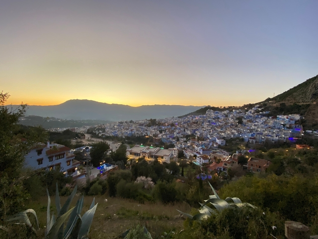 A panoramic view of Chefchaouen with mountains in the background at sunset.