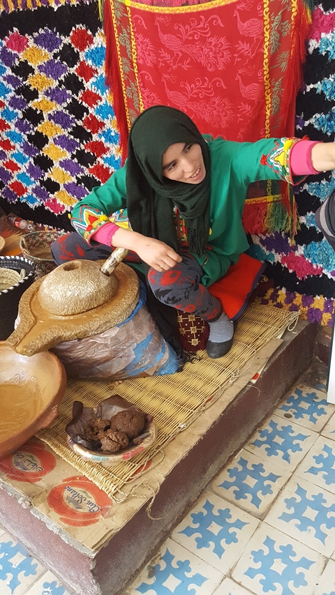 A person using a traditional stone grinder, surrounded by colorful fabrics.