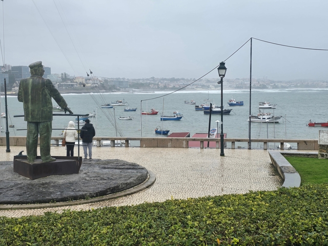 Statue near a harbor with boats on a cloudy day.