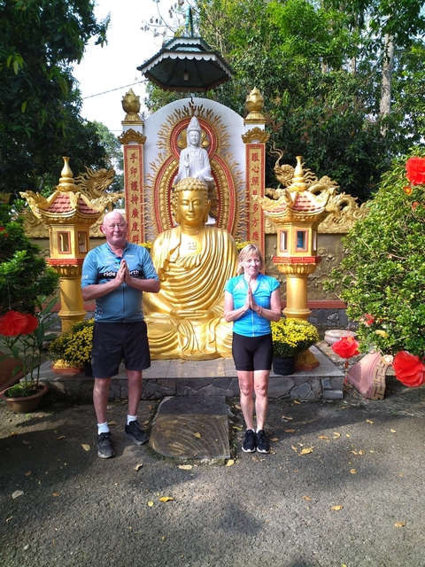       Two people posing in front of a golden Buddha statue.
  
