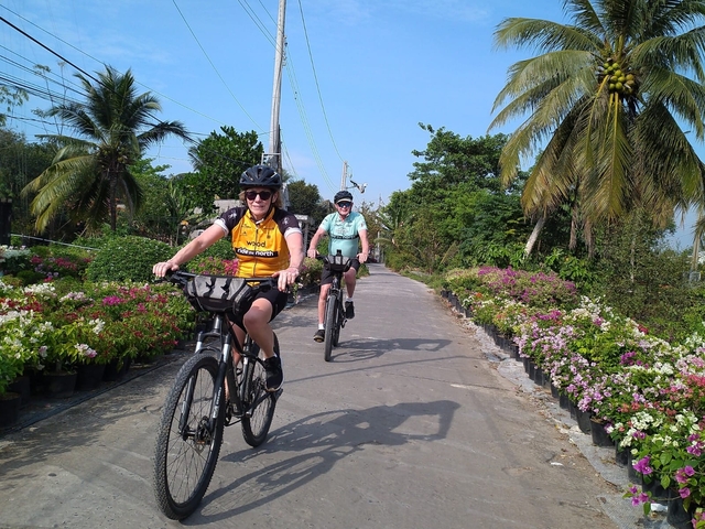 Two people biking on a path surrounded by plants.