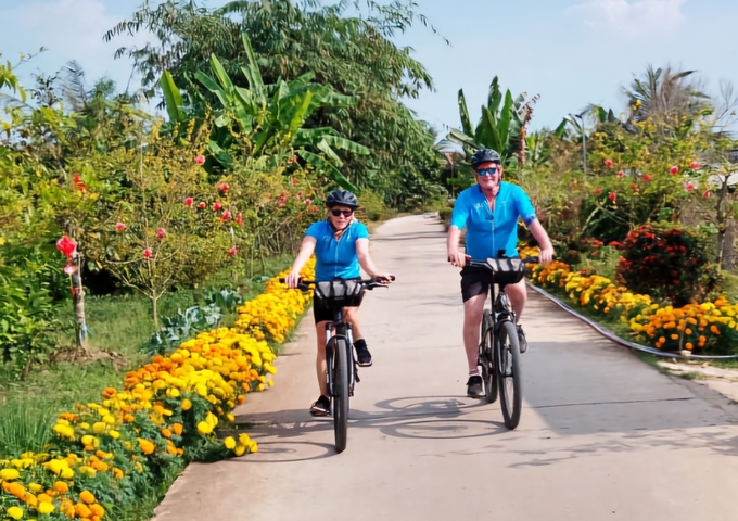 Two people biking on a scenic path lined with flowers.