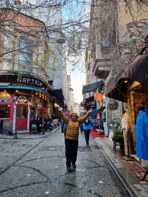       Person posing in a vibrant street with shops and colorful buildings.
  