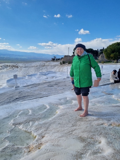       Person standing on travertine terraces with a scenic backdrop.
  
