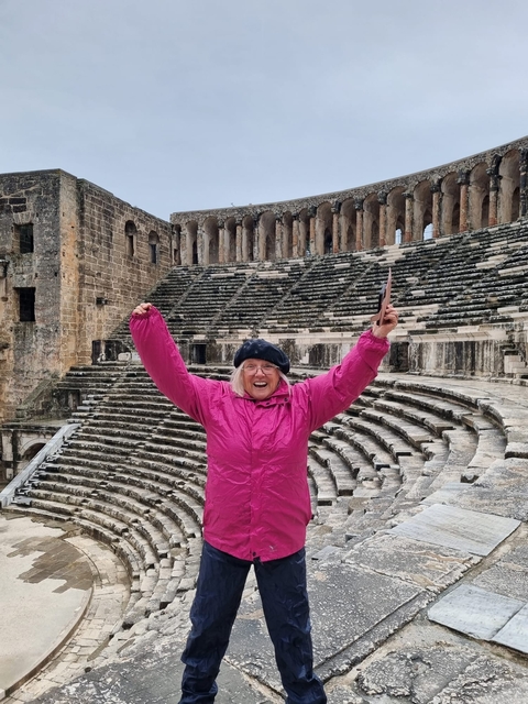       A person in a bright pink jacket standing in an ancient amphitheater with stone seats.
  