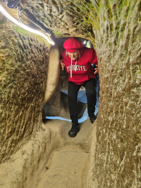       A person navigating through narrow stone passages wearing a red hoodie.
  