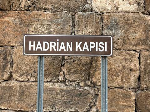       A sign reading 'HADRIAN KAPISI' in front of a stone wall.
  