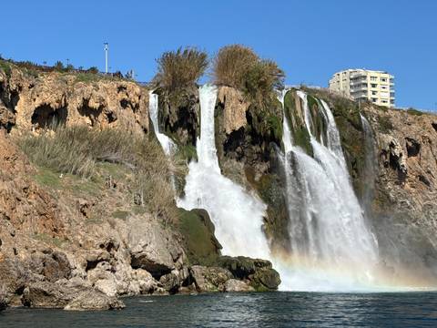       Waterfall cascading over a rocky cliff with buildings in the background.
  