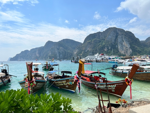 Traditional longtail boats in a turquoise bay with mountains in the background.