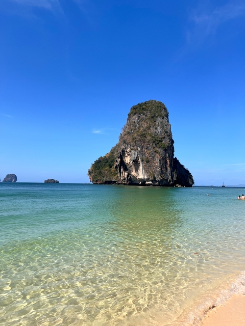       Large rock formation in turquoise waters near a beach.
  