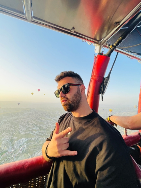 Man in a hot air balloon basket with balloons in background.