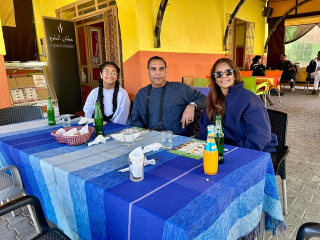       Three people sitting at a table outdoors with beverages and menus.
  