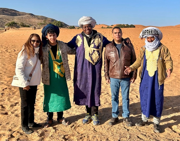       Five people in traditional clothing posing in a desert landscape.
  