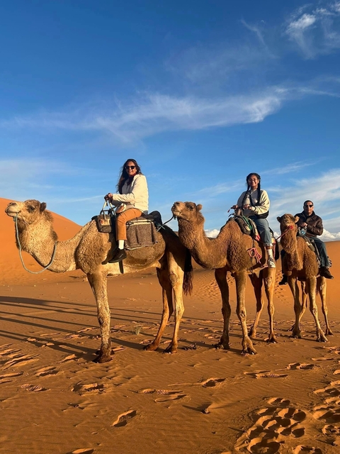       Three people riding camels in a desert setting.
  