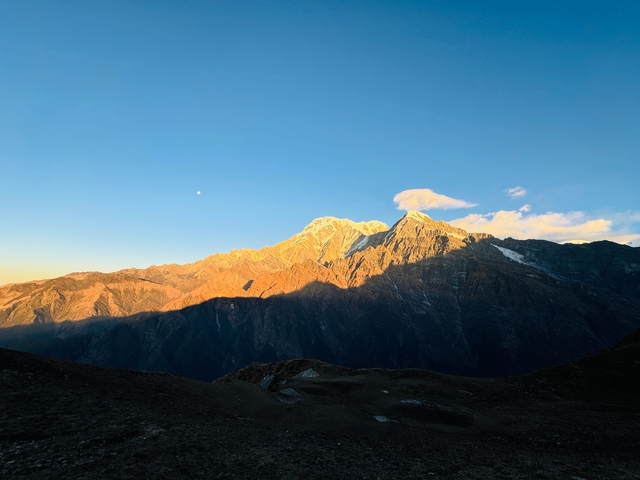 Sunlit mountains with a clear sky casting dark shadows.
