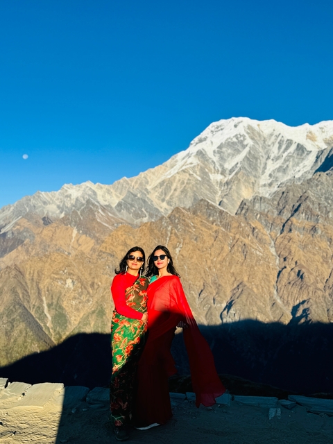Two people posing in colorful clothing with mountains behind.