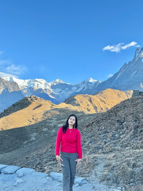 Person in traditional attire posing in front of sunlit mountains.