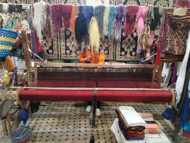       A person working on a traditional weaving loom with colorful textiles.
  