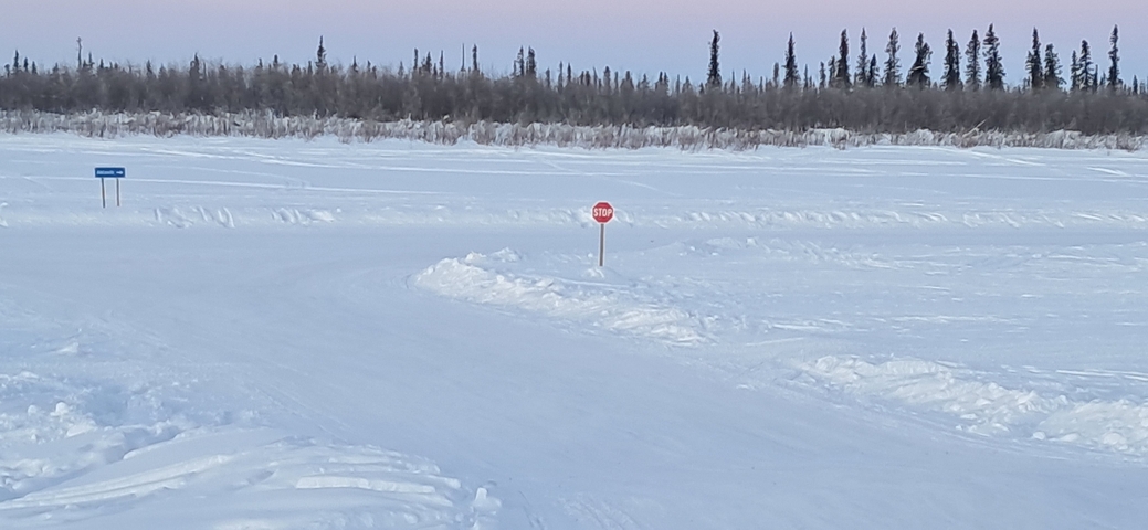 Snow-covered road intersection with small stop sign.