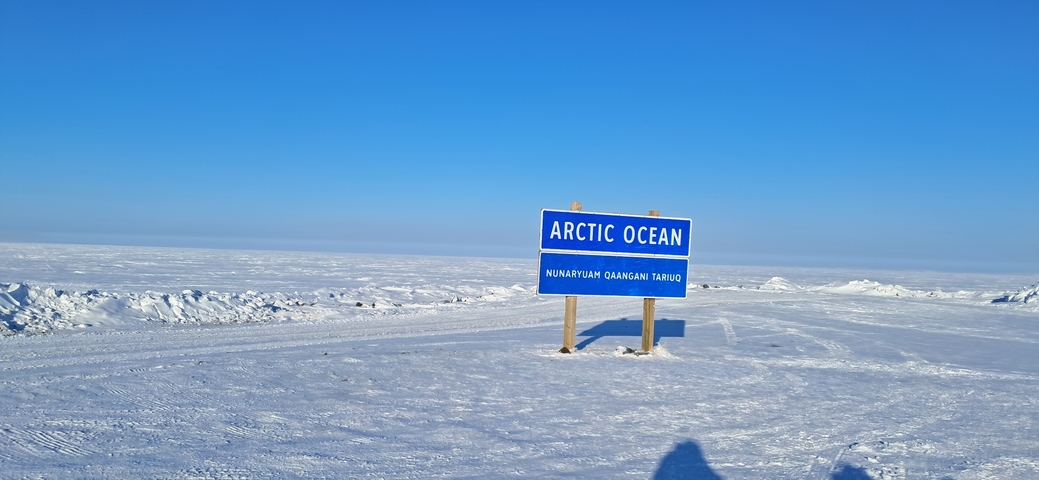 Sign indicating location near Arctic Ocean with snowy surroundings.