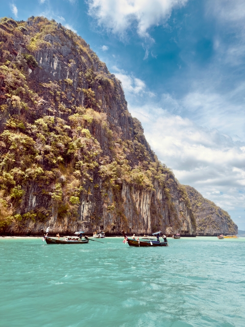       Tall cliff face covered in foliage against a blue sky.
  