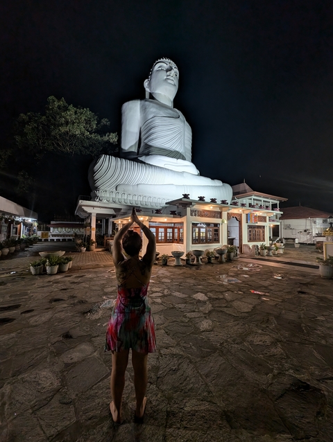       Person meditating in front of a giant Buddha statue at night.
  