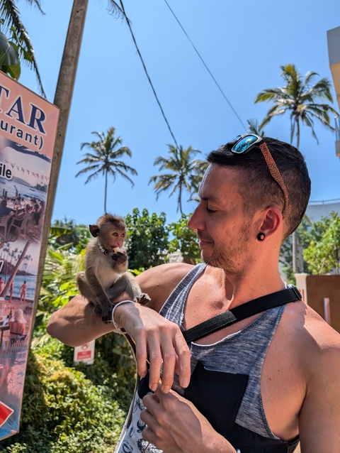 Man holding a baby monkey with palm trees in the background.