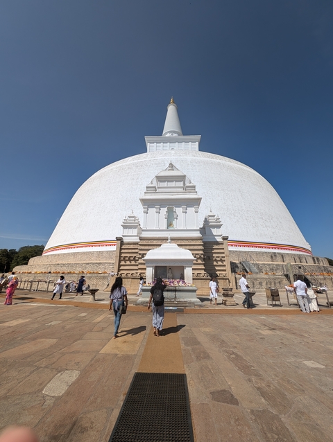 Giant white stupa with people walking around it.