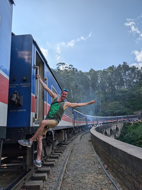 Person hanging playfully out of a moving train with a forest background.