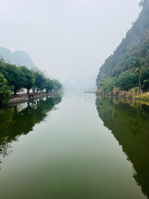       A peaceful river flanked by trees with mountains in the mist.
  