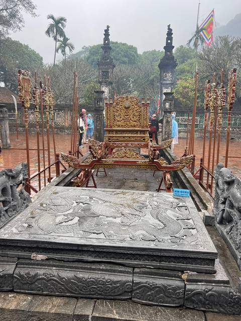       An ornate throne in a historical site with people examining the carvings.
  