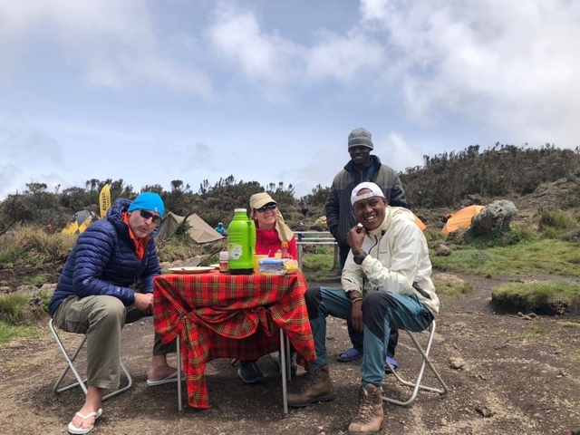 A group of people enjoying a meal at a campsite with tents in the background.