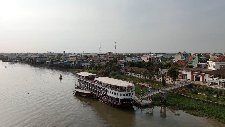 A riverboat docked by a riverbank with buildings in the background.