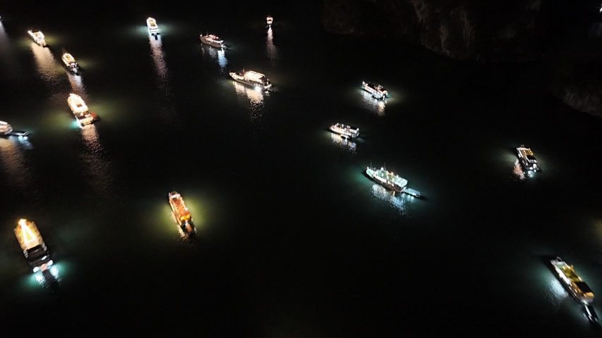 Numerous boats with lights suspended on water seen at night.