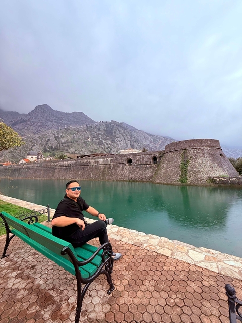       Tourist sitting by a scenic water body with fortifications.
  