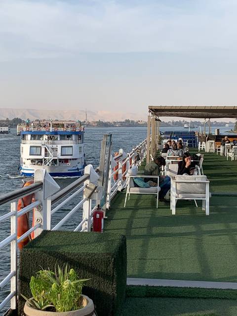       Cruise ship on a river with passengers onboard, city in the background.
  