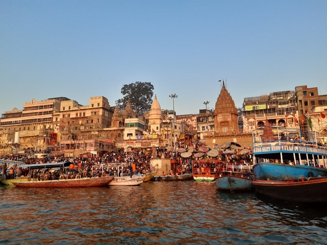 A busy waterfront in the evening with boats and illuminated buildings.