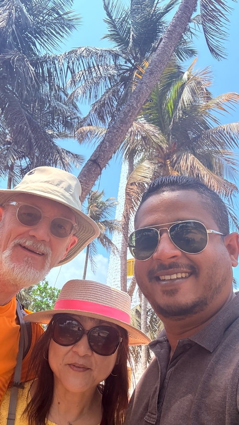 Two men taking a selfie with palm trees in the background.