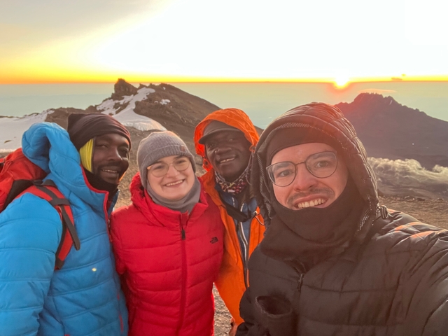 People posing at a mountain summit at sunrise.