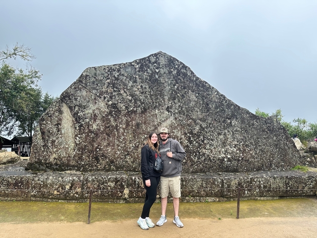 Two people in front of a large stone monolith.