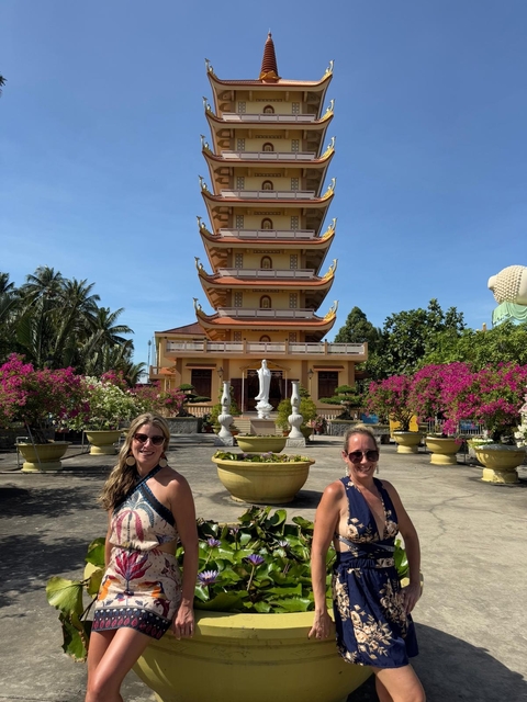 Two women posing in front of a pagoda with bright flowers.