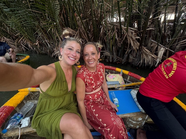 Two women in traditional attire on a boat with lush vegetation.