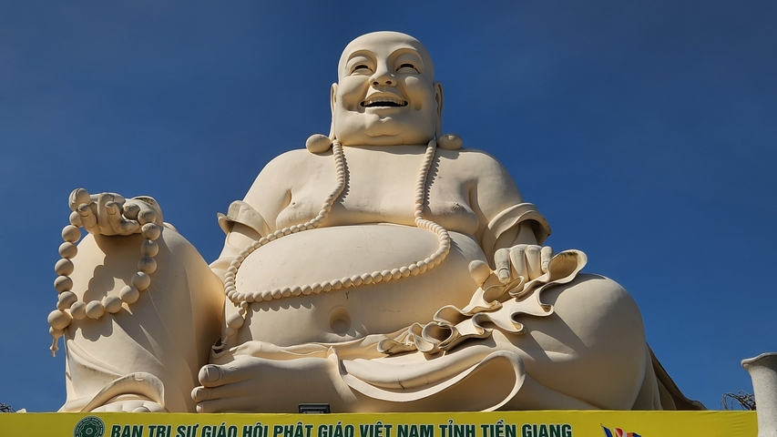 Large smiling Buddha statue under clear blue sky.