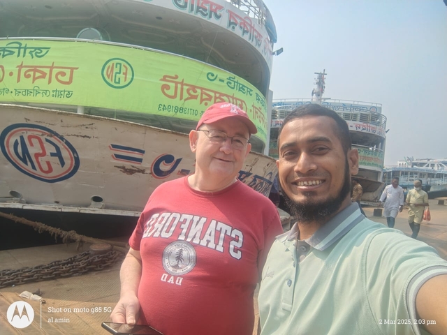 Two men posing in front of boats in a harbor setting.