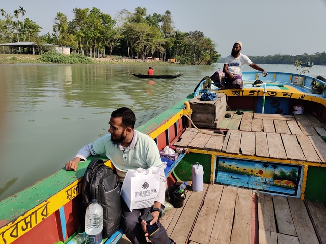 Men on a boat in a green river surrounded by forests.