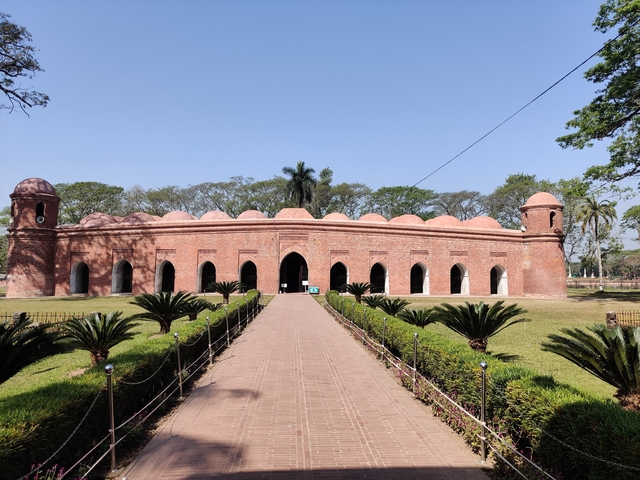       A historical building with arches and greenery in the foreground.
  
