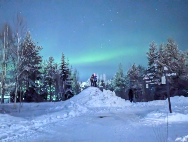 Two people standing on snow with the northern lights in the background.