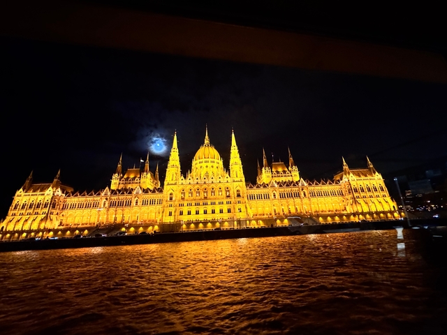 Illuminated Parliament Building at night with a moon behind.
