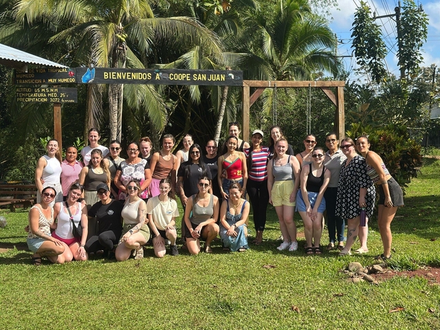 A group of people posing under a welcome sign in a tropical setting.