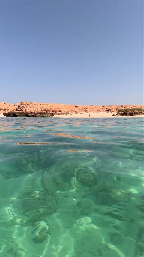      Clear turquoise waters with a distant beach and people.
  
